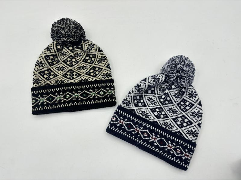 Twee Fair Isle gebreide pompon-mutsen met Scandinavisch sneeuwvlokpatroon in zwart-crème en marineblauw-wit op witte achtergrond.