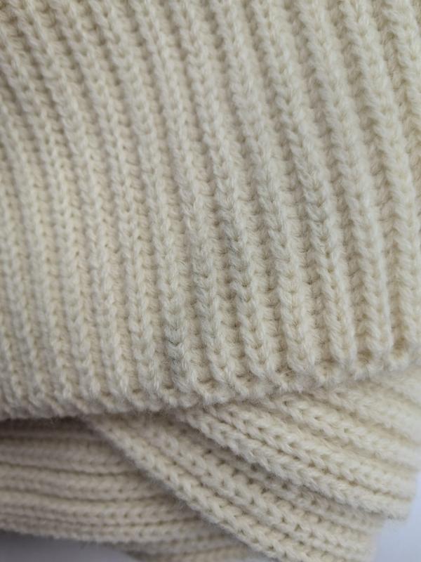 Close-up van een crèmekleurige grofgebreide plaid met ribbeltextuur en gevouwen lagen
