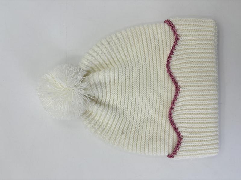 Crème gebreide wintermuts met pluizige pompon en roze zigzagsteek rand.