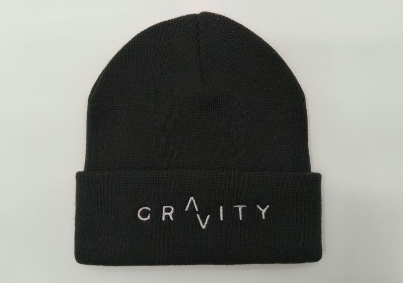 Zwarte geribbelde gebreide muts met omgeslagen rand en wit geborduurd GRAVITY-logo op witte achtergrond.