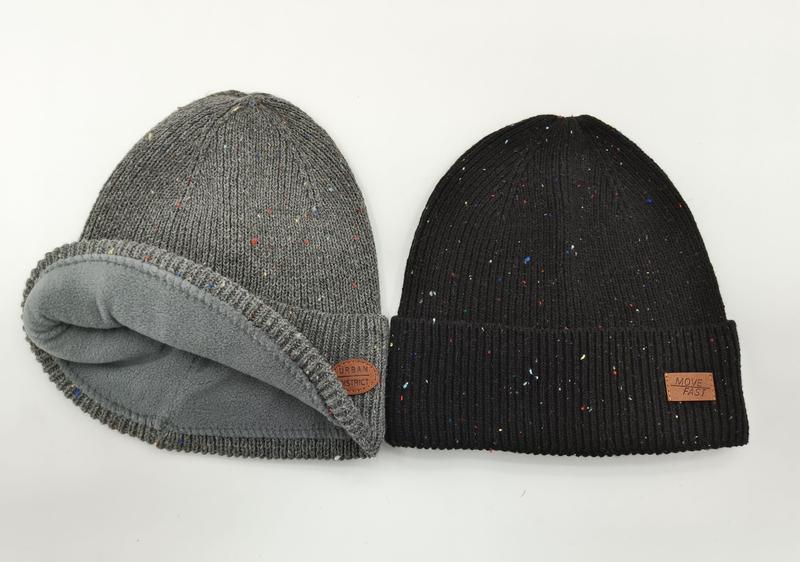 Twee gespikkelde gebreide wintermutsen: grijze fleece-gevoerde en zwarte geribbelde muts met leren patch.
