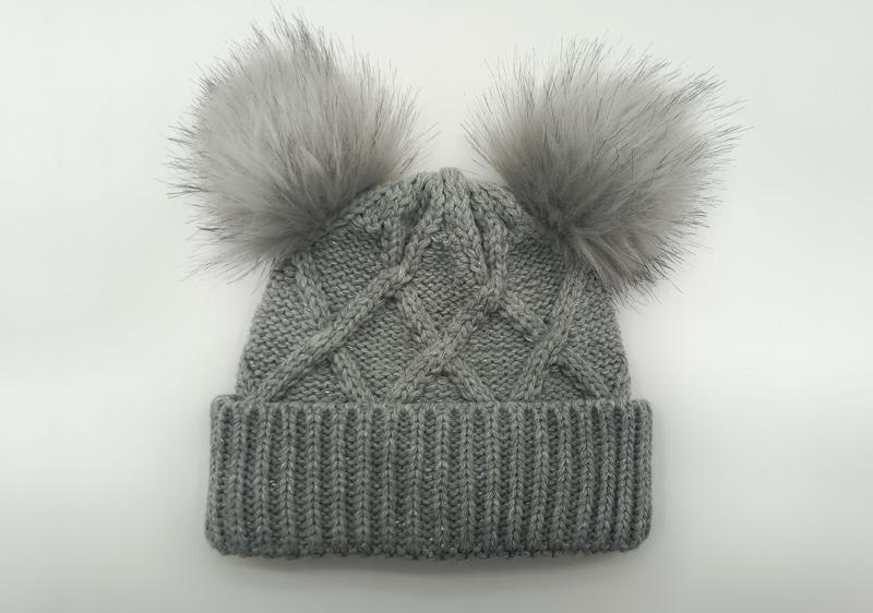 Grijze kabelgebreide wintermuts met twee pluizige neppbont pompons