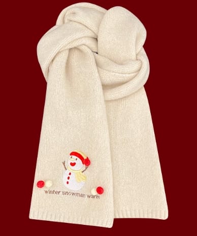 Crème gebreide wintersjaal gevouwen met geborduurde sneeuwpop en rode pompons op donkerrode achtergrond.