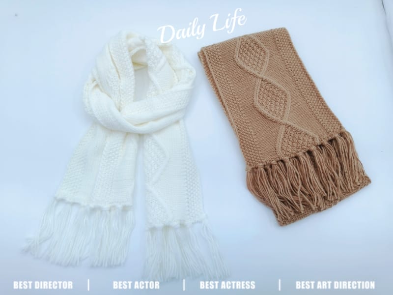 Twee gebreide wintershawls met franjes: crèmewitte omslagdoek en gevouwen kameelbruine kabelgebreide sjaal op witte achtergrond.