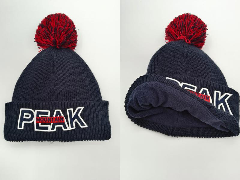 Marineblauw geribde gebreide muts met rode pompon en geborduurd PEAK MOUNTAIN-logo op omgeslagen rand.