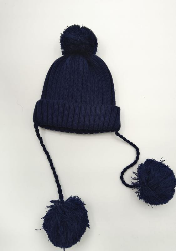 Donkerblauwe geribbelde gebreide wintermuts met pompom op top en twee lange gevlochten banden met grote pompoms.