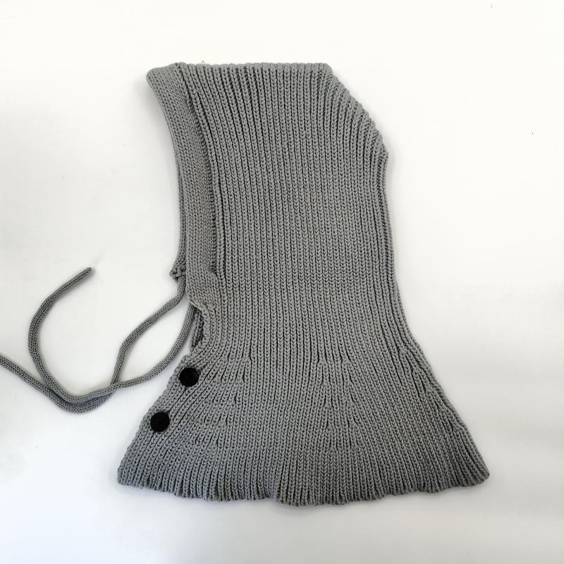 Grijze geribbelde gebreide balaclava met verstelbare koordjes en twee zwarte knoopsluiting op witte achtergrond.