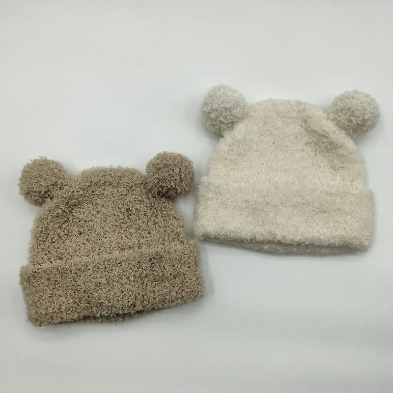 `Twee pluizige gebreide babymutsen met berensoren en pompon in beige en crème op witte achtergrond.`