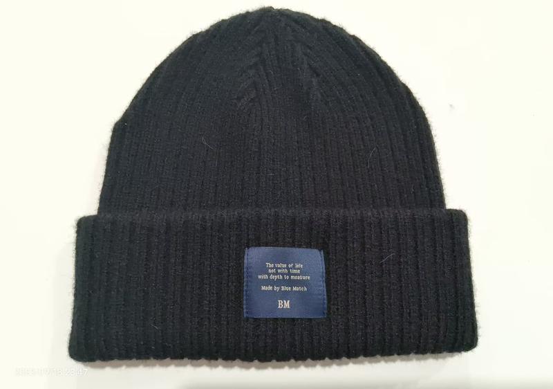 Zwarte geribbelde gebreide wintermuts met omgeslagen rand en blauw geweven labelpatch – groothandel winteraccessoires.