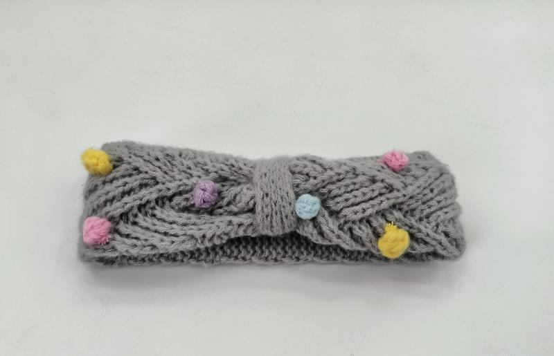 Grijze kabelgebreide hoofdband met gekleurde pompons in geel