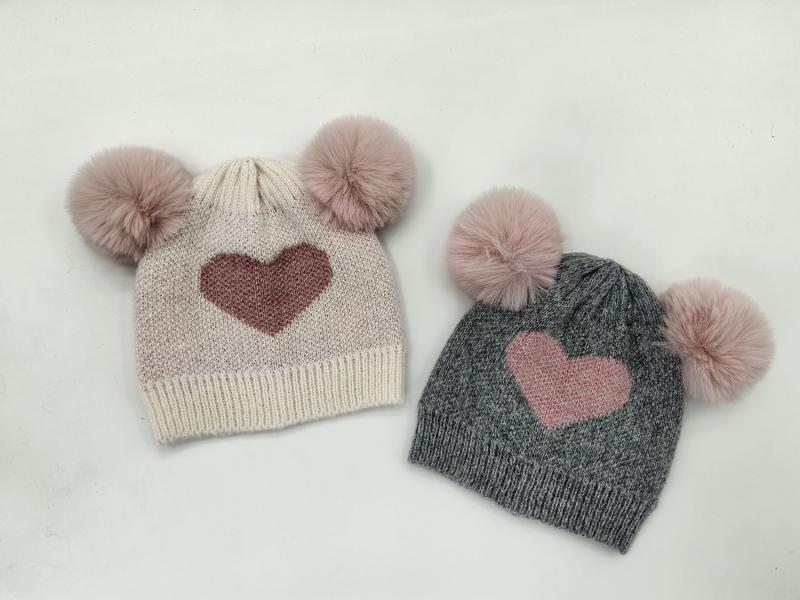 Twee gebreide kindermutsen met dubbele pompons en hartmotief