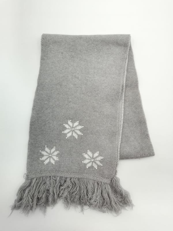 Gevouwen grijze gebreide plaid met witte sneeuwvlokken en franjes op witte achtergrond.