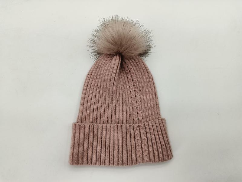 Roze geribbelde gebreide wintermuts met grote nepbont pompon op witte achtergrond.