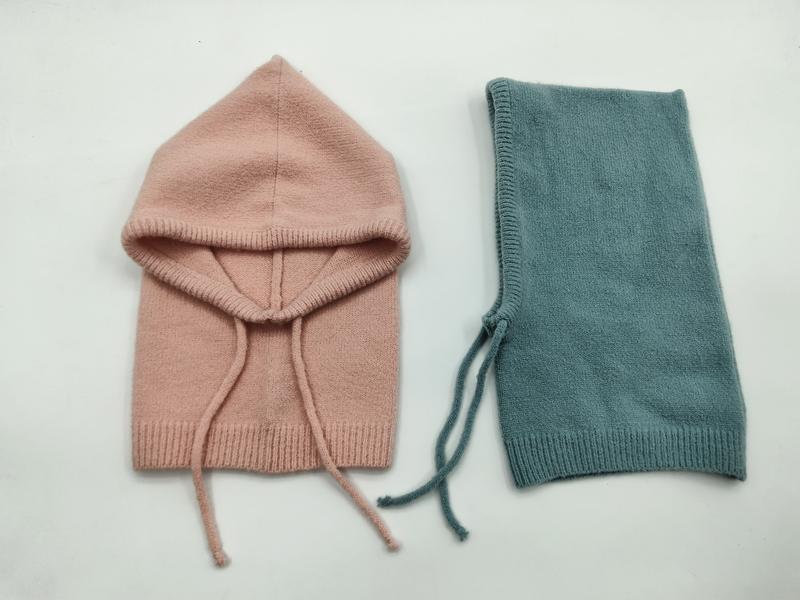 Twee gebreide baby-bivakmutsen plat neergelegd: één blush roze met open kap en één gevouwen teal