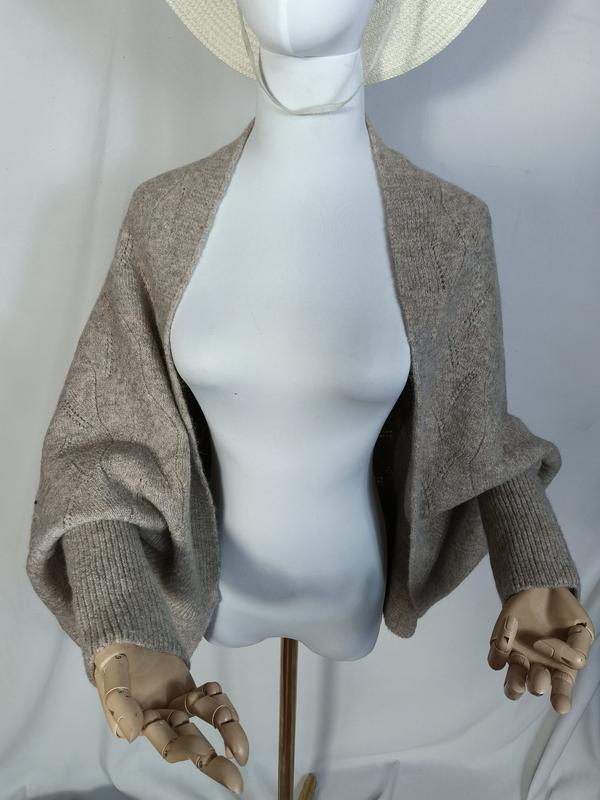 Taupe gebreide open shrug met ballonmouwen en geribbelde manchetten op een mannequin.