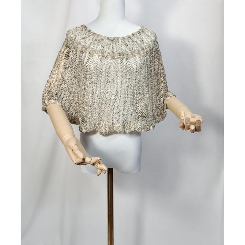 Beige goudkleurige metallic open gebreide gehaakt cropped poncho top op witte mannequin met houten handen.