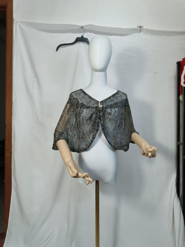 Blauwe en gouden metallic open-gebreide cape shawl op witte mannequin met parelknoop sluiting.