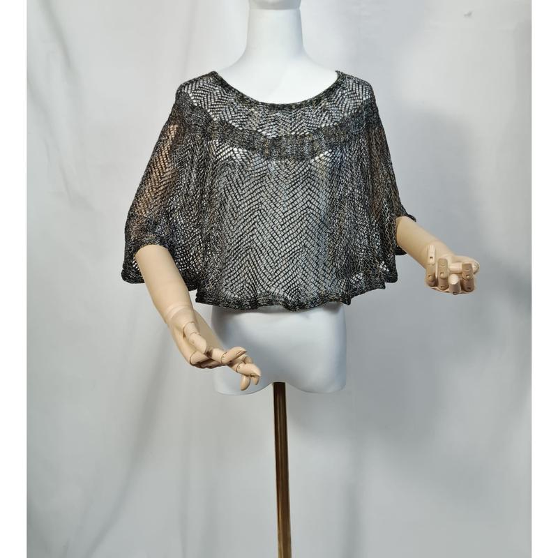 Metallic zilveren en zwarte open-gebreide cropped cape poncho op witte mannequin met houten armen.
