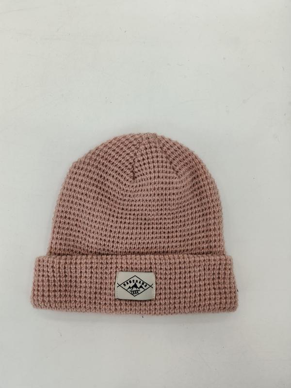Stoffig roze wafelgebreide beanie muts met omgeslagen rand en geweven labelpatch op witte achtergrond.