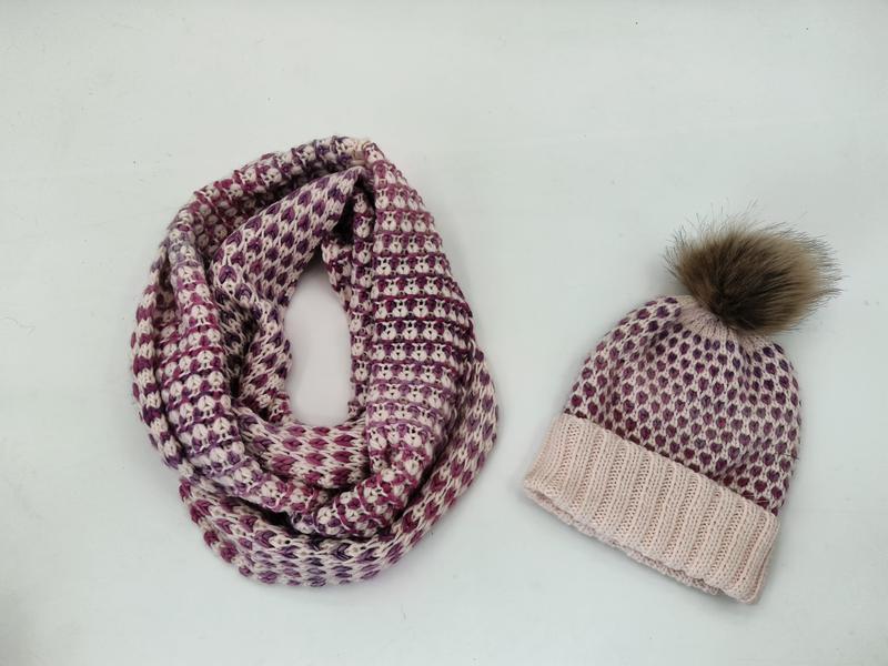 Bijpassende gebreide winterset met paarse en crème sjaal en muts met pompon op witte achtergrond.