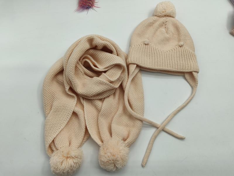 Crème gebreide kindermuts met oorflappen en pompon