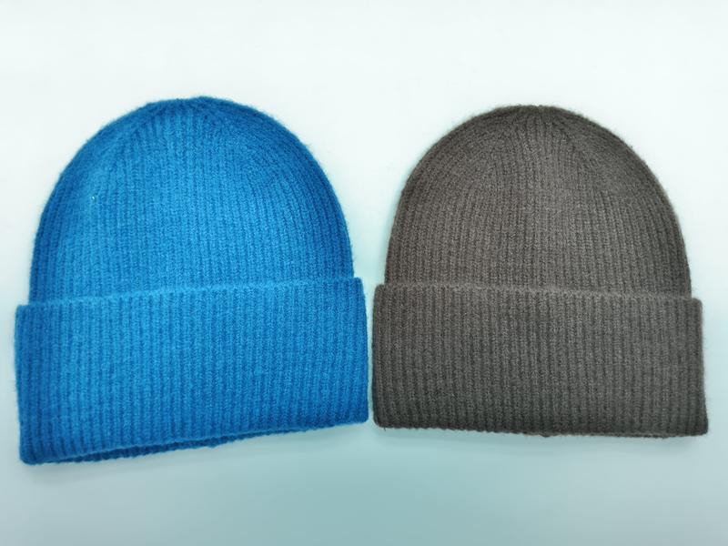 Twee geribbelde gebreide muts met omslag naast elkaar – één in helder blauw en één in taupe bruin op witte achtergrond.