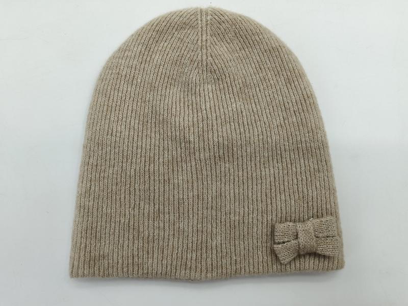 Beige geribbelde gebreide muts met kleine gebreide strik aan de zijkant
