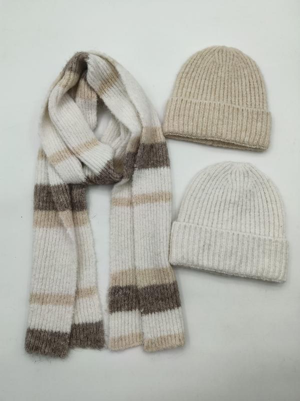 Twee ribgebreide mutsen in beige en crème met bijpassende gestreepte gebreide sjaal in neutrale tinten op witte achtergrond.