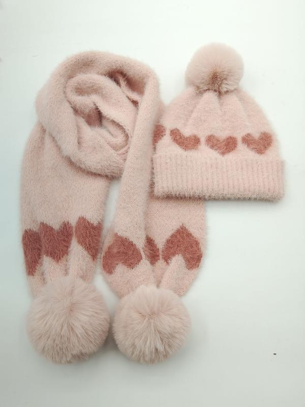 Roze gebreide wintermuts en sjaal set met hartjespatroon en pompons op witte achtergrond.