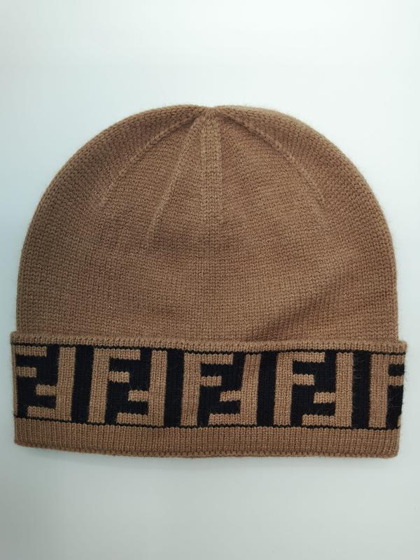 Camelkleurige gebreide beanie muts met omgeslagen rand en herhalend zwart geometrisch monogrampatroon.