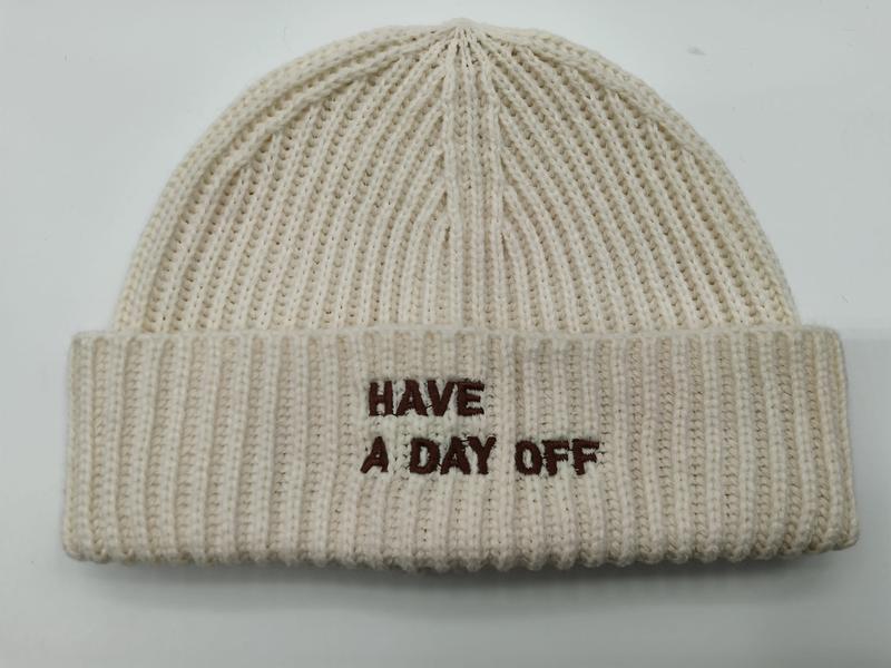 Crème grofgebreide beanie muts met omgeslagen rand en geborduurd bruine tekst 'Have A Day Off'.