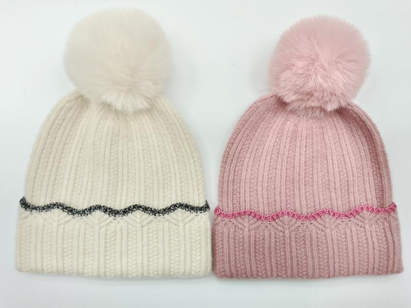Twee ribgebreide pompon-mutsen naast elkaar: crème met zwart glitterrand en roze met roze glitterrand