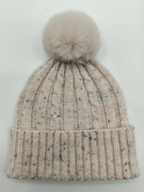 Crème gebreide wintermuts met gekleurde vlekjes en grote pluizige nepbont pompon bovenop.