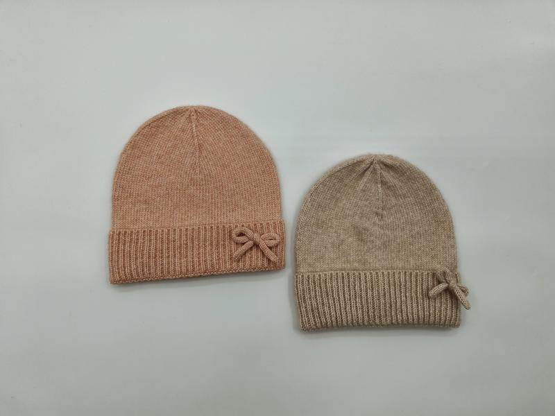 Twee gebreide mutsen met geribbelde rand en strikdetail in blush roze en beige