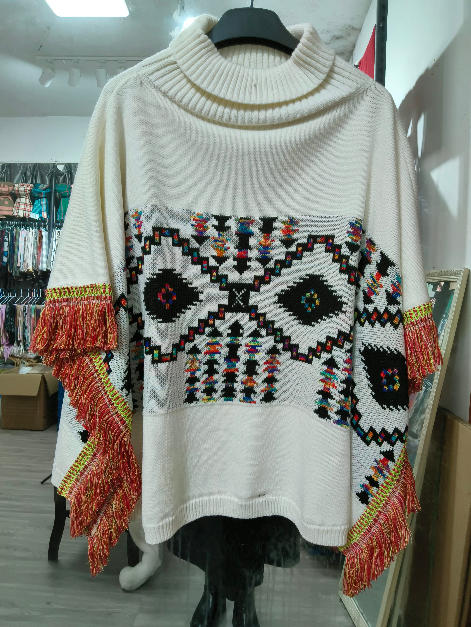 Crème gebreide col-poncho met multicolor Azteeks patroon en rode franje-mouwen op paspop.