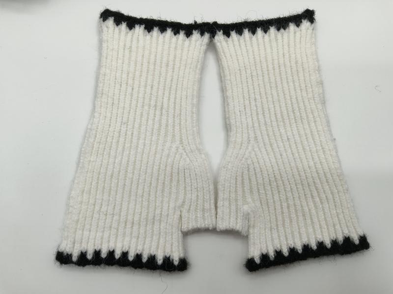 Plat neergelegde handgebreide witte ribbelpatroon vingerloze wanten met zwarte contrastbies aan manchetten.