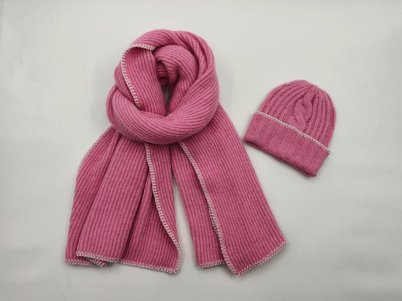 Roze geribbelde gebreide wintersjaal en bijpassende muts met witte contraststeek op witte achtergrond.