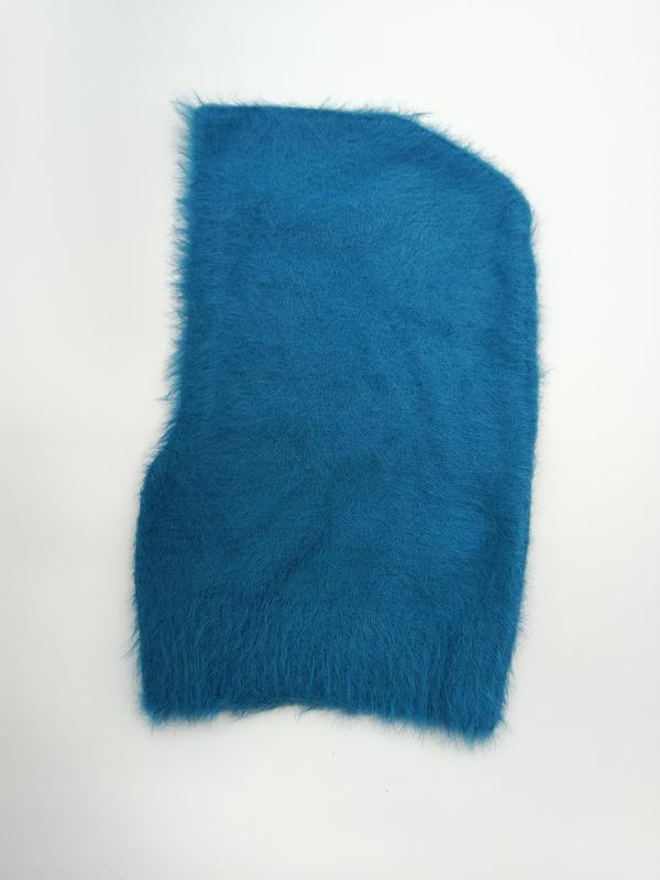 Teal blauwe pluizige gebreide bivakmuts plat neergelegd op witte achtergrond