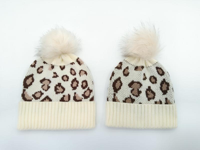 Twee crème luipaardprint gebreide mutsen met imitatiebont pompon, voor volwassenen en kinderen, witte achtergrond.