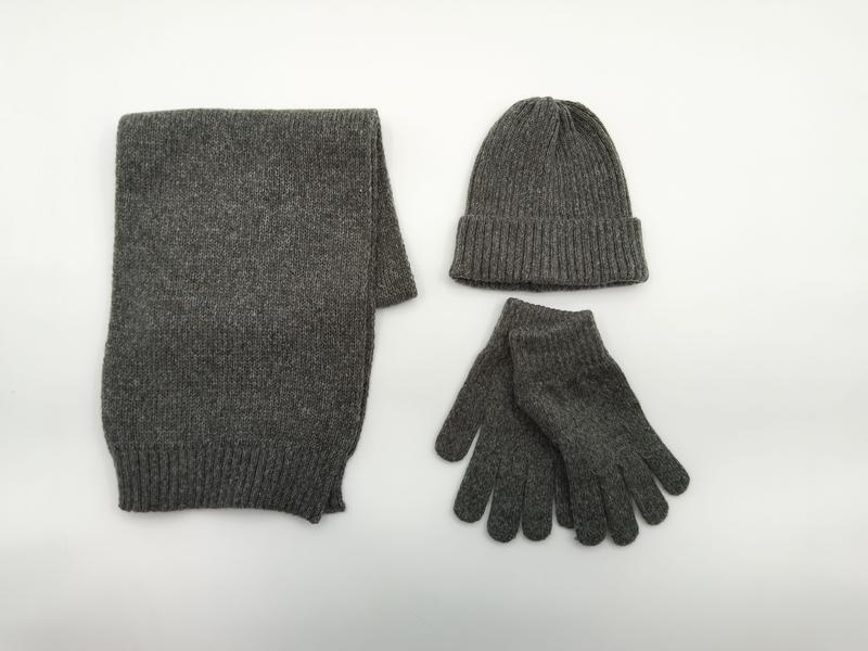 Grijze gemêleerde gebreide winterset met gevouwen sjaal, geribbelde muts en handschoenen op witte achtergrond.