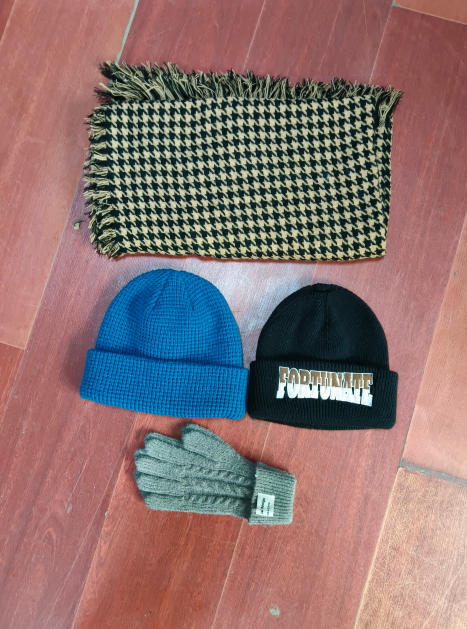 Platte lay van een beige-zwarte houndstooth franjessjaal, blauwe wafelgebreide muts, zwarte muts en grijze kabelgebreide handschoenen.