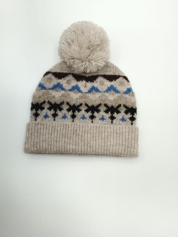 Havermoutkleurige gebreide muts met Fair Isle sneeuwvlokpatroon in blauw en zwart, met een pluizige crèmekleurige pompon.