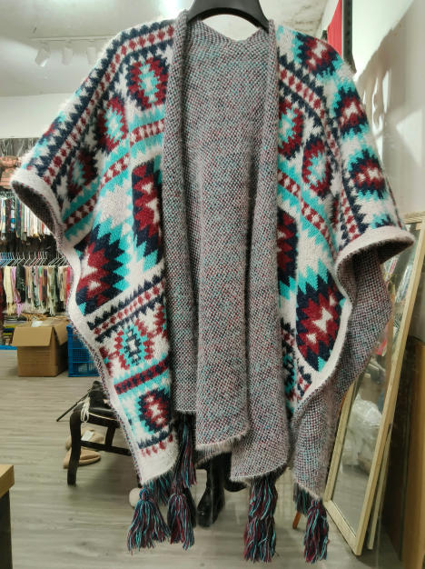 Grijze gebreide poncho met aztec patroon in teal, bordeaux en wit, open voorkant en kwastenfranje zoom.