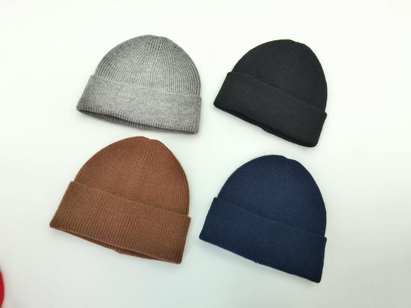 `Vier geribbelde gebreide beanie mutsen met omgeslagen rand in grijs, zwart, bruin en marineblauw op witte achtergrond.`