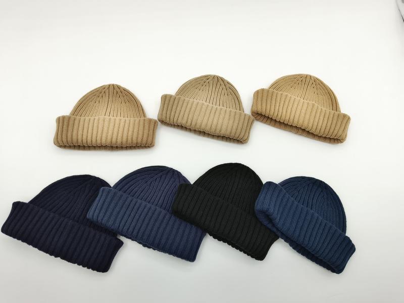 Zeven geribbelde gebreide muts met omgeslagen rand in beige, marine, zwart en blauw op witte achtergrond.