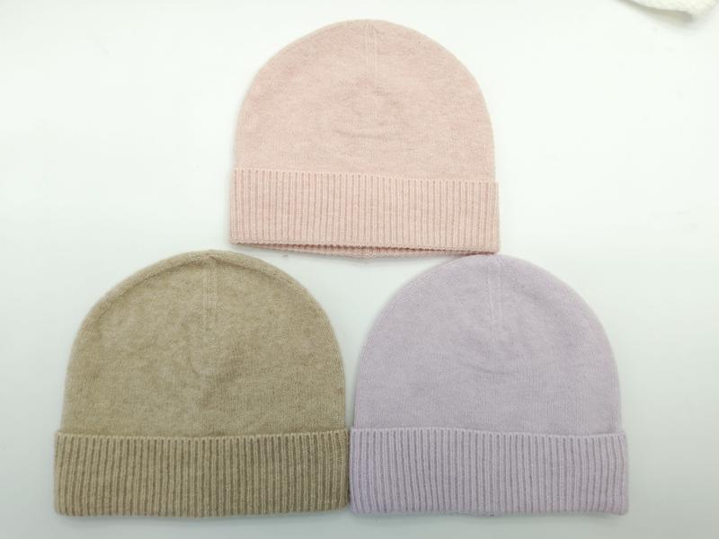 Drie gebreide mutsen plat neergelegd in roze, taupe beige en lavendel met geribbelde manchetten op witte achtergrond.
